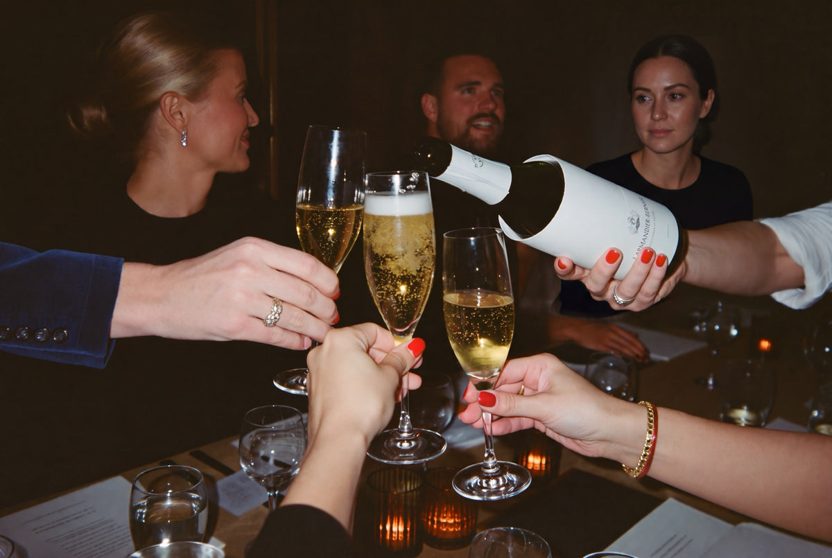 Guests raising flutes of Champagne as a bottle of Larmandier-Bernier is poured at a candlelit dinner