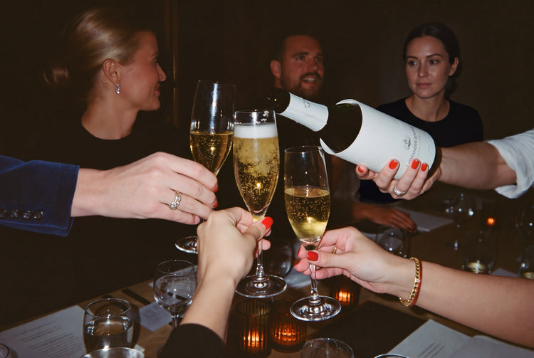 Guests raising flutes of Champagne as a bottle of Larmandier-Bernier is poured at a candlelit dinner