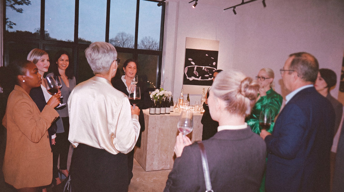 Guests with glasses of wine listen to a host at a standing reception